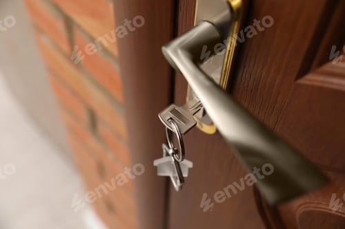 Preview: Key with house-shaped trinket in door lock, closeup. Space for text