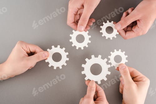 Preview: cropped view of people holding white gears on grey background