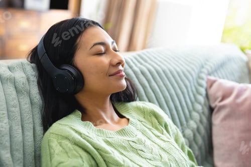 Preview: Image of happy biracial woman in headphones relaxing on sofa with eyes closed at home, copy space