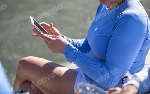 Preview: A woman sitting outdoors looking at her cell phone wearing a long sleeve blue shirt