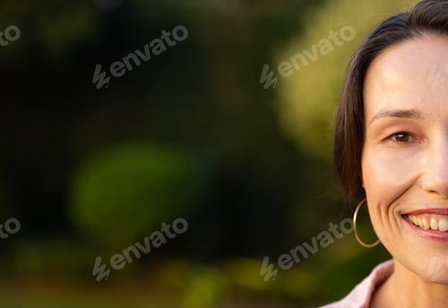 Preview: Smiling middle-aged woman with hoop earring enjoying outdoor time in garden setting, copy space