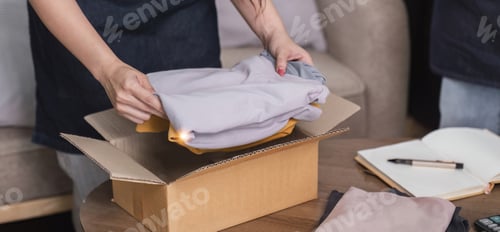 Preview: Close-up shot of a young woman packing a shirt into a box to deliver the product to a customer.