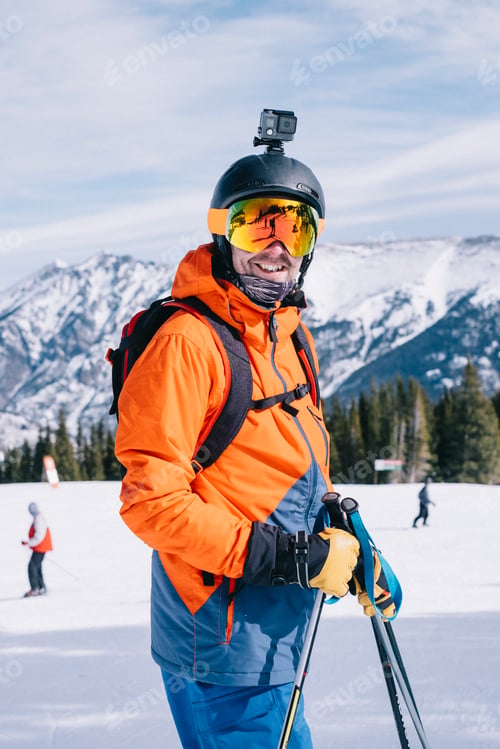 Preview: A man in orange ski jacket, with a head cam and helmet.