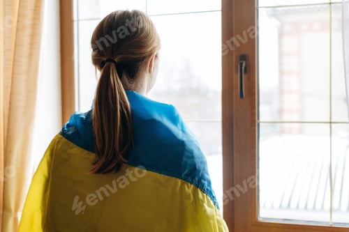 Preview: Back view of the blonde woman wrapped in Ukraine flag looking out of the window