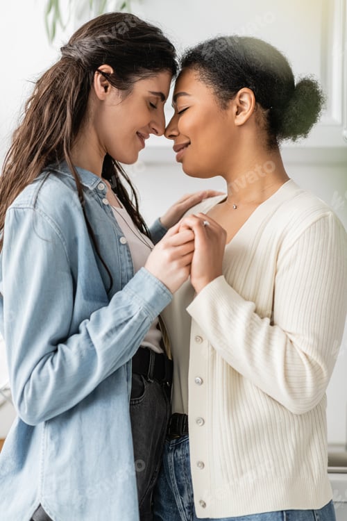Preview: side view of multiracial woman with engagement ring on finger holding hands with girlfriend