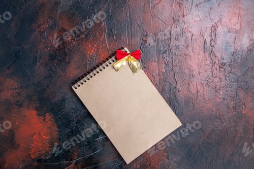 Preview: top view a notepad with little bow on dark red table with copy place