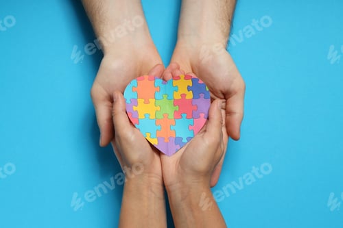 Preview: Heart made of puzzles in hands on blue background, top view