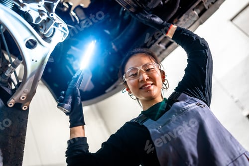 Preview: Female mechanic inspecting car with flashlight in workshop