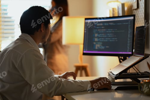 Preview: Focused software developers man programming on desktop computer in dark office