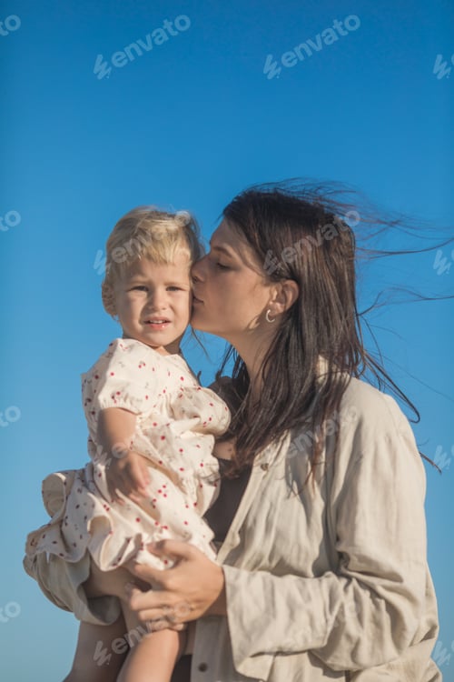 Preview: Smiling mother and beautiful daughter having fun on the beach. Portrait of kid embracing her mom