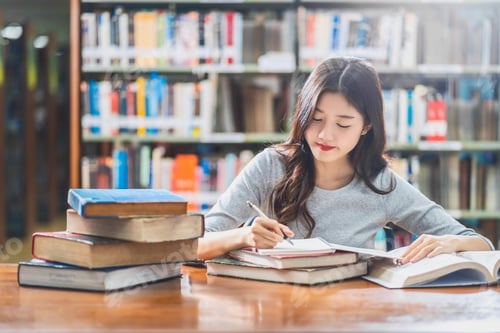 Preview: Asian young Student in casual suit reading and doing homework in library of university or colleage