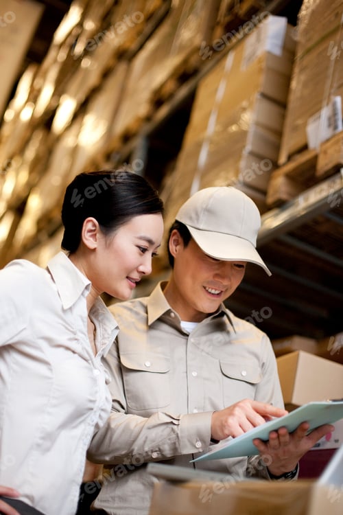 Preview: Chinese businesswoman in a warehouse with worker using a laptop