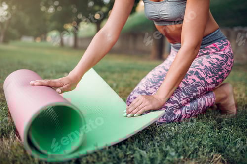 Preview: Young woman rolling yoga mat in park