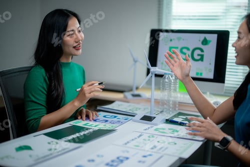 Preview: Two businesswomen discussing esg strategy using documents and computer in office