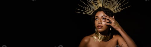 Preview: tattooed african american woman with golden crown and paint on face looking up isolated on black,