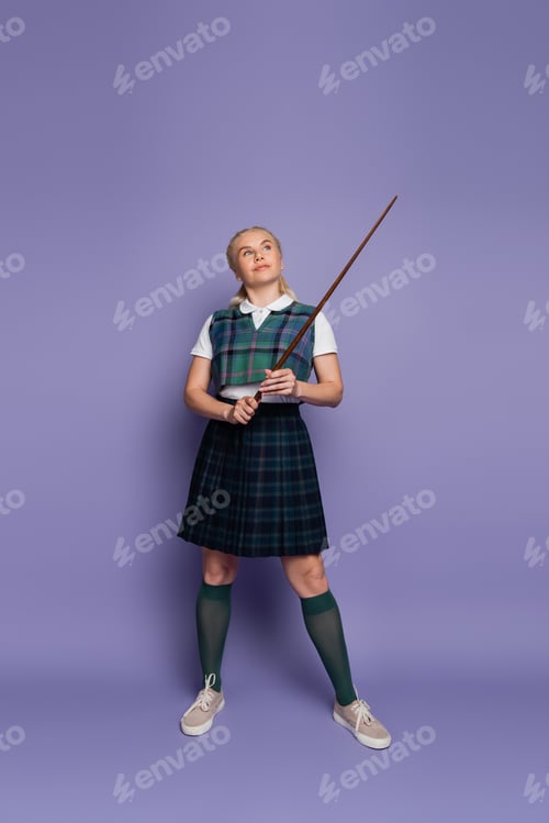 Preview: Full length of student in uniform holding pointer on purple background