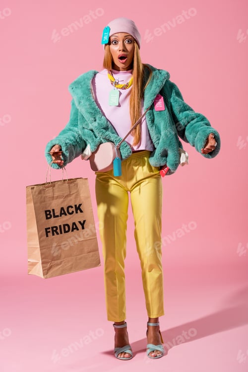 Preview: shocked, stylish african ameican girl holding shopping bag with black friday inscription on pink