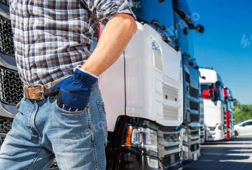 Preview: Trucker in Blue Jeans Standing Near Transport Semi Trucks on a Sunny Day