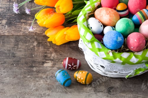 Preview: Colorful easter eggs resting in basket near vibrant tulips on rustic wooden table