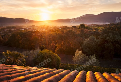 Preview: View of mountainous landscape over rooftops at sunset.