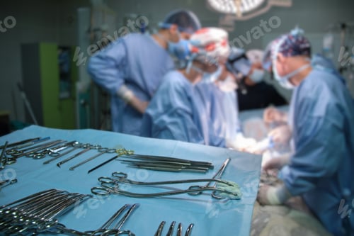 Preview: Closeup of surgical tools on table and team of surgery doctors operating a patient in hospital room