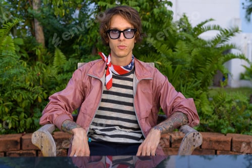 Preview: Young handsome rebellious man sitting outdoors and looking at camera