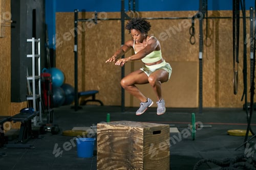 Preview: Black sportswoman jumping on box during workout