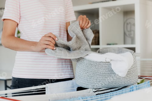 Preview: Woman hanging clean wet clothes laundry on drying rack at home laundry room