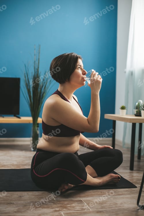 Preview: Young woman doing fitness exercises and drinking water at home.