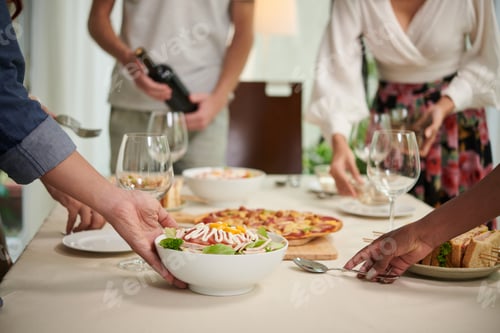Preview: Close-up of young friends putting bowls of salad and other snacks on table