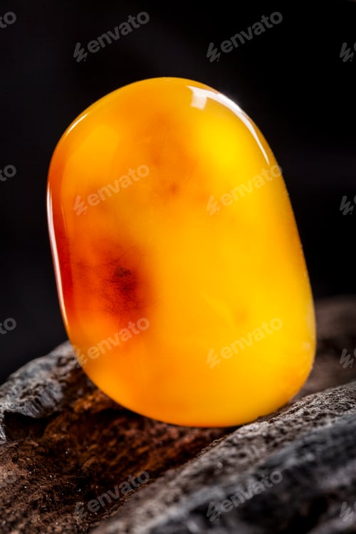 Preview: Natural amber. A piece of yellow opaque natural amber on large piece of dark stoned wood
