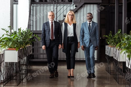 Preview: confident blonde businesswoman walking with handsome multicultural partners in office
