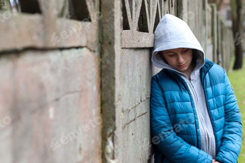 Preview: Sad teen boy 11 years old wearing gray hoodie and blue jacket in outdoors. Depressed mood.