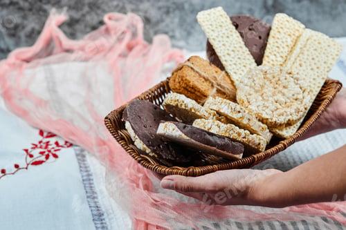 Preview: Hand holding a basket of mixed biscuits on a marble background