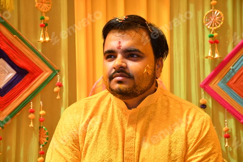 Preview: Man in orange attire at a vibrant Haldi ceremony against a yellow backdrop