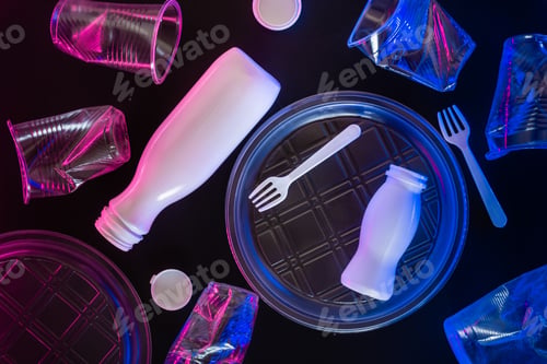 Preview: Plastic transparent tableware in neon lighting on black background. Environmental pollution concept