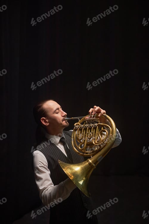 Preview: Passionate Male Musician Playing French Horn in Spotlight on Stage against Black