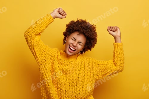 Vista previa: Accomplishment and success concept. Joyful Afro woman raises arms, feels glad and relaxed, tilts hea