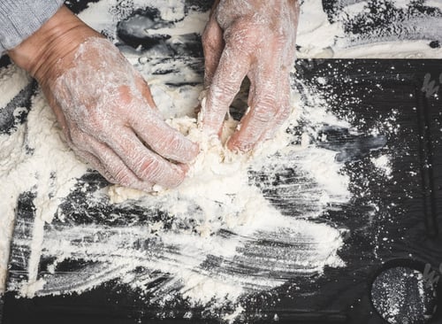 Preview: two female hands knead the dough from white wheat flour on a black table, top view
