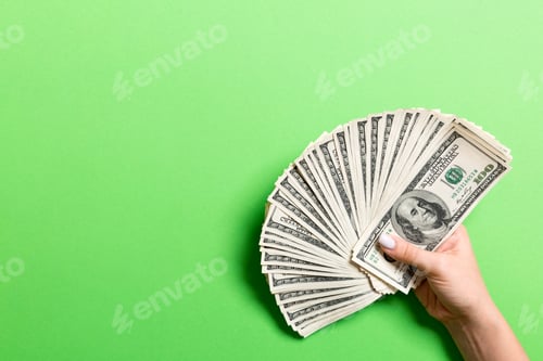 Preview: Top view of female hand holding a fan of one hundred dollars on colorful background