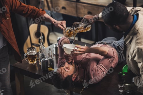 Preview: cropped shot of friends pouring beer in funnel and man drinking while lying on table