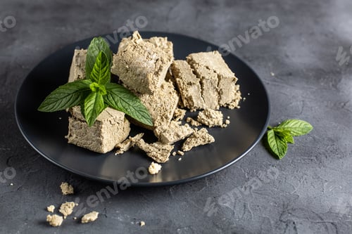 Preview: Pieces of halva on black plate. Sweet dessert with mint leaves on black background