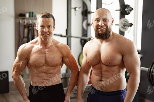 Preview: Two shirtless men standing in gym. Young man and his senior father exercise together in gym