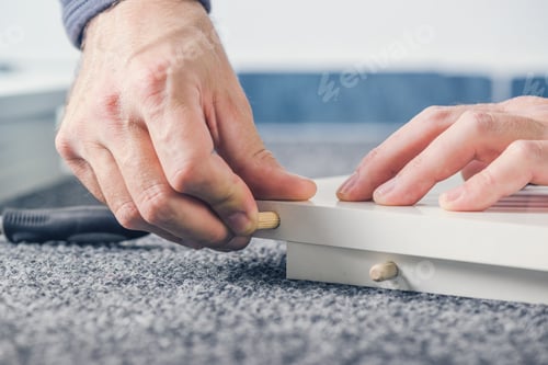 Preview: Man assembling furniture at home, hand with wooden dowel pins