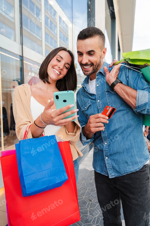 Preview: Vertical. Couple using a shopping online smartphone app to buy a sale on a mall. Young customers