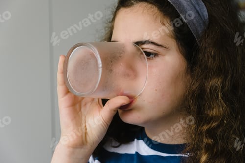 Preview: Young girl drinking water and eating at home with smartphone on the table