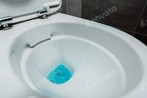 Preview: close up view of blue liquid detergent in ceramic clean toilet bowl in modern restroom with grey