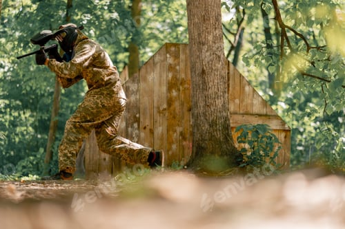 Preview: in the wild near tree structures player in a pintball uniform holds a pistol with a blue balloon
