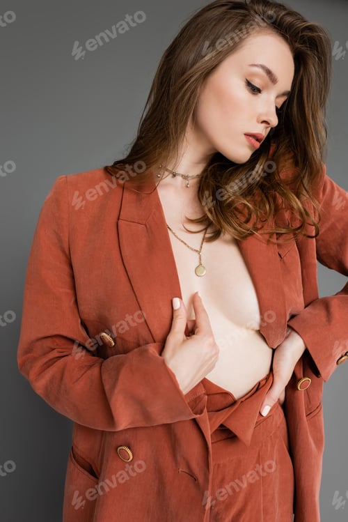 Preview: sexy young woman with brunette and wavy hair posing in trendy and oversize suit with terracotta