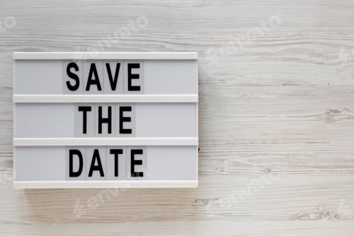 Preview: 'Save the date' words on a modern board on a white wooden surface, top view.